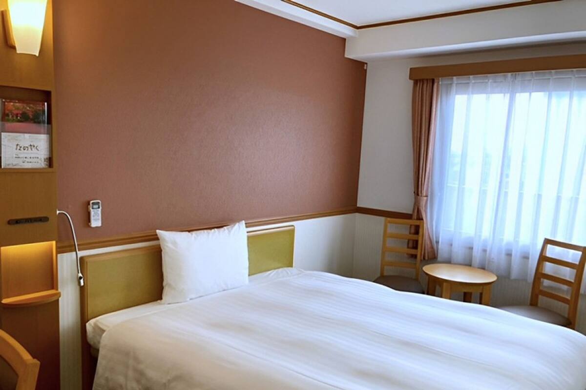 A hotel room with a large bed, a bedside table, a chair, and a window with curtains.