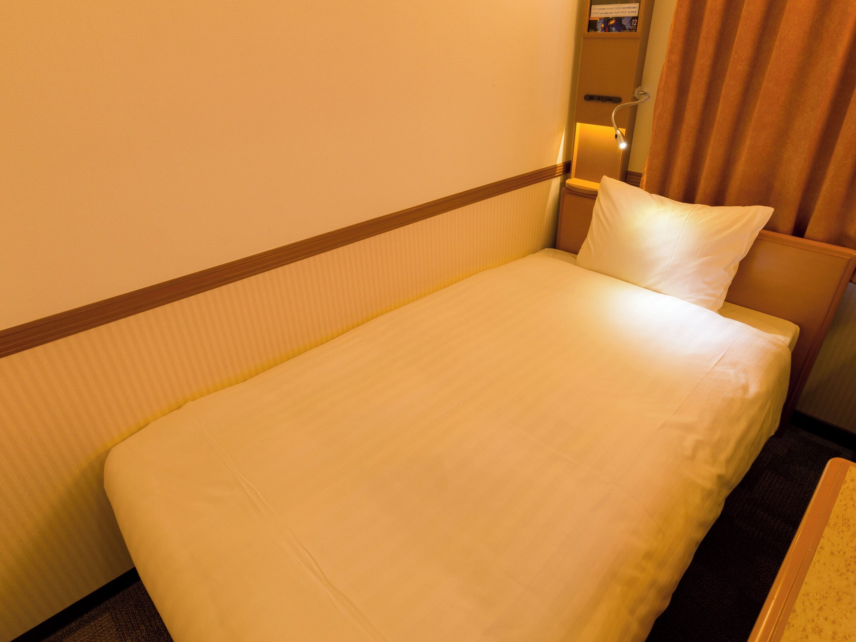 A single bed in a hotel room with a headboard, a nightstand, and a lamp.