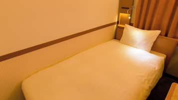 A single bed in a hotel room with a headboard, a nightstand, and a lamp.