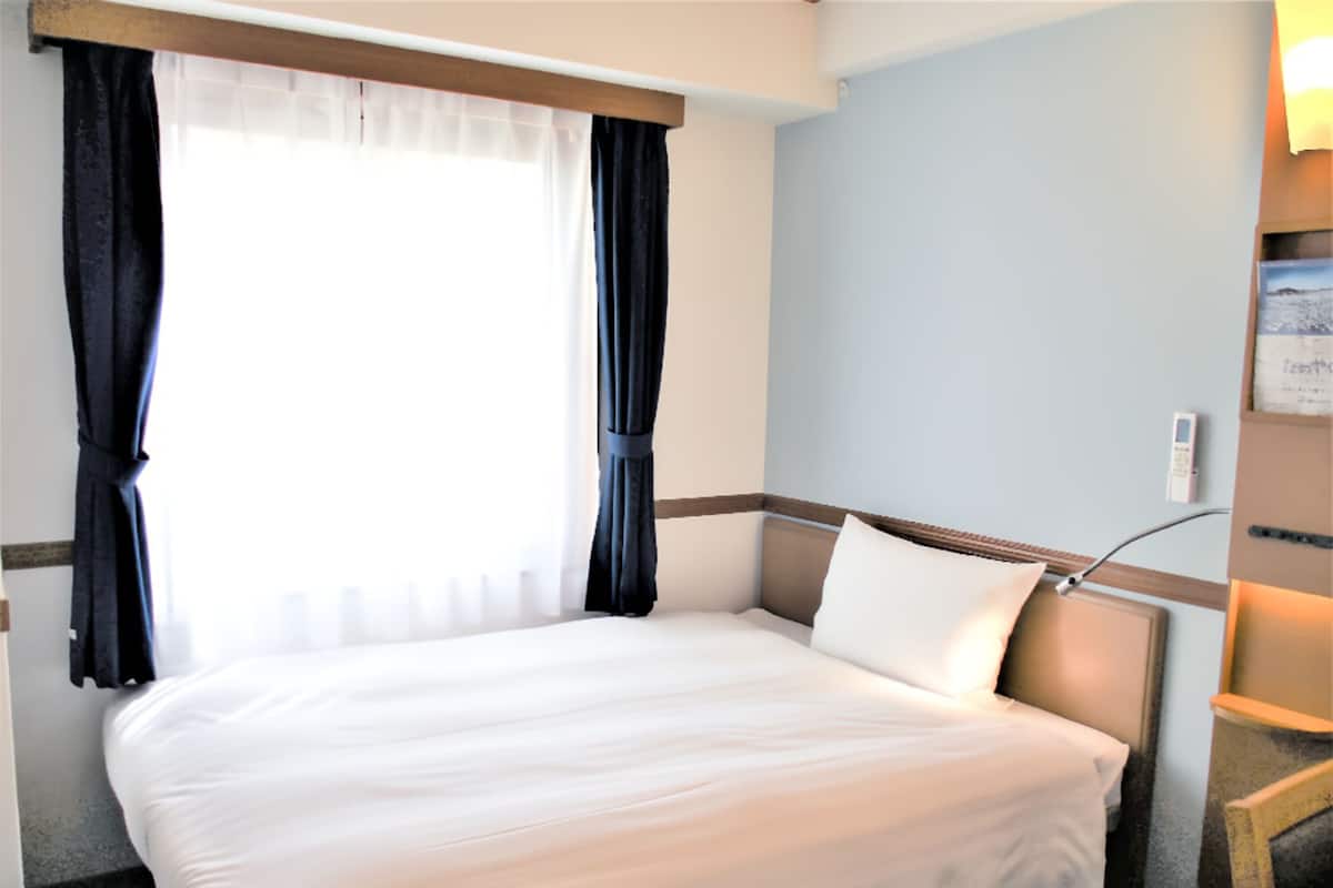 A hotel room with a bed, curtains, a bedside table, and a wall-mounted lamp.