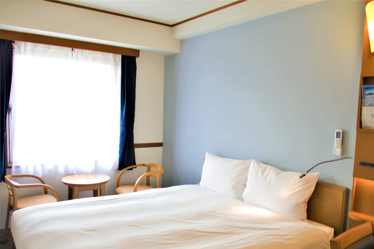 A hotel room with a large bed, two chairs, a small table, and a window with curtains.