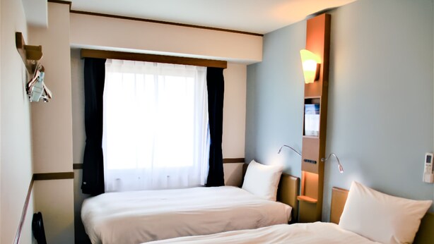 A hotel room with two beds, a window with curtains, a bedside table, and a wall-mounted lamp. - Toyoko Inn Tokyo Korakuen Bunkyokuyakusho Mae (Tokyo)