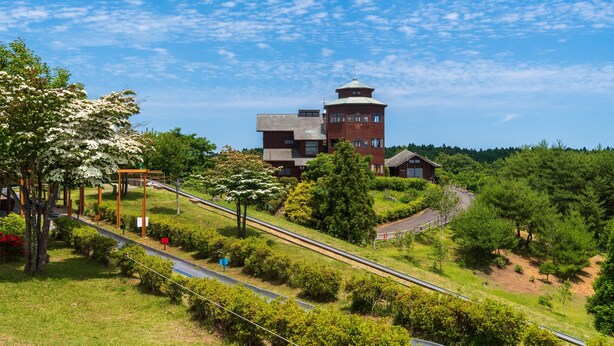 A building with a tower, surrounded by greenery and a railway track. - Toyoko Inn Hitachi Ekimae (Hitachi)