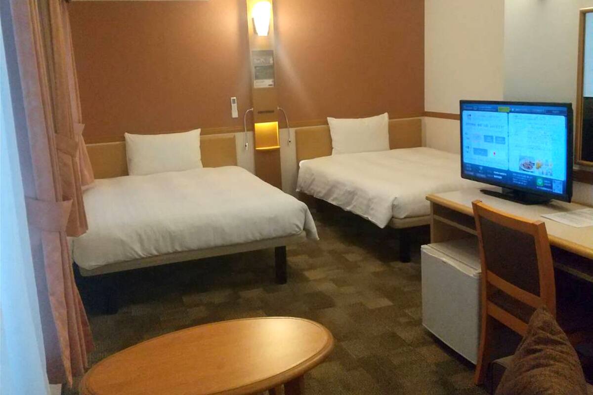 A hotel room with two beds, a desk with a computer, a small table, and a chair.