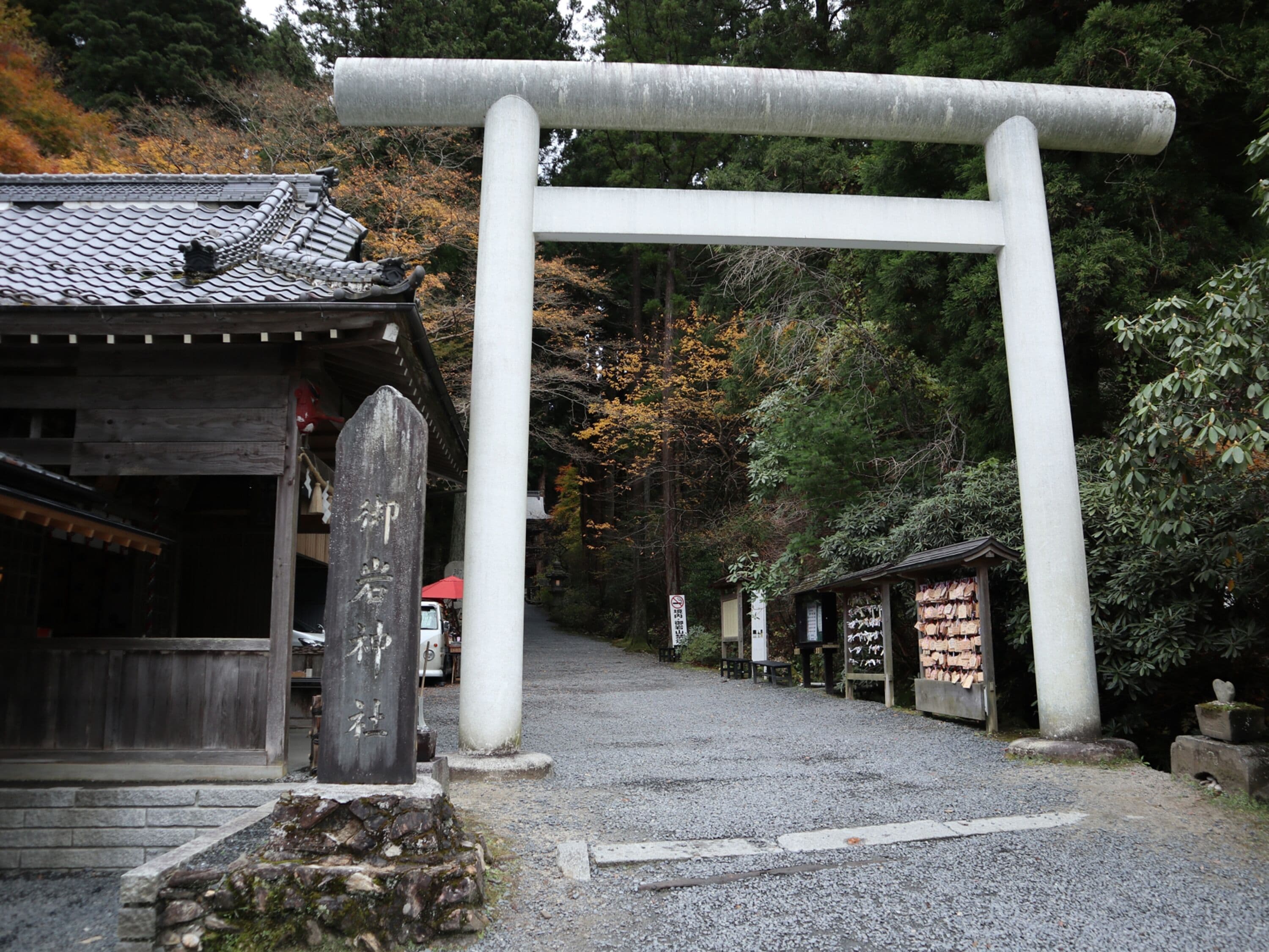A traditional Japanese torii gate at the entrance of a shrine, with a wooden building and a stone lantern nearby.