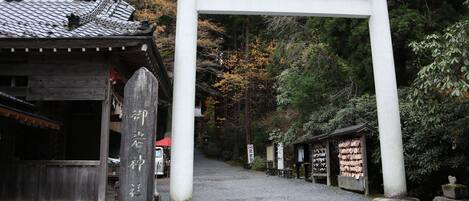 A traditional Japanese torii gate at the entrance of a shrine, with a wooden building and a stone lantern nearby.