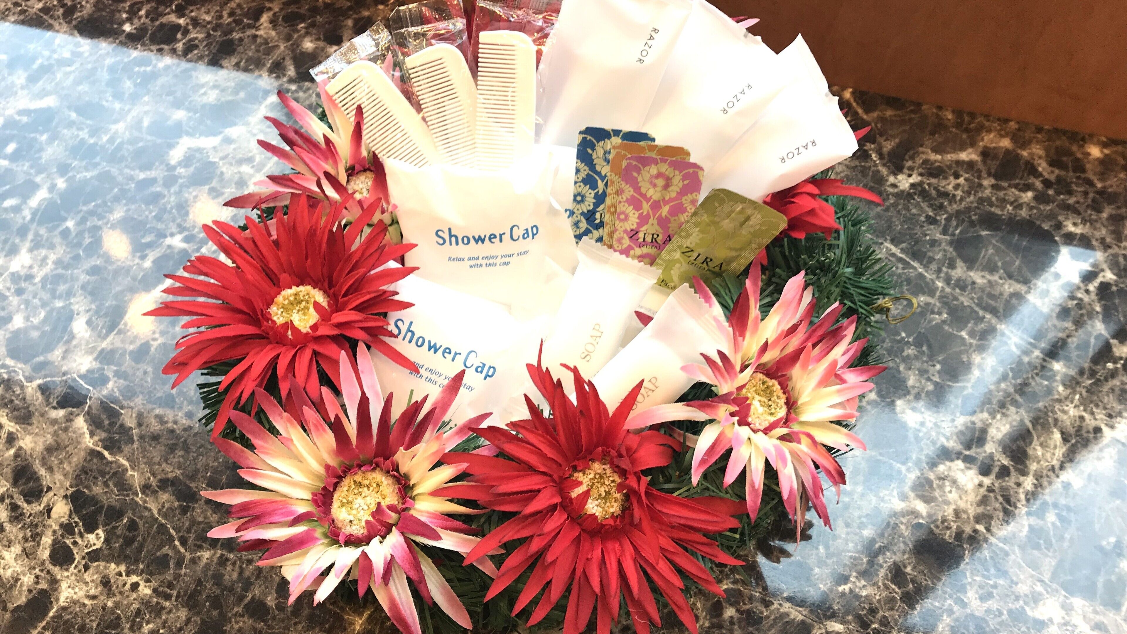 A floral arrangement with red and yellow flowers, a shower cap, and a ZIRA gift card.