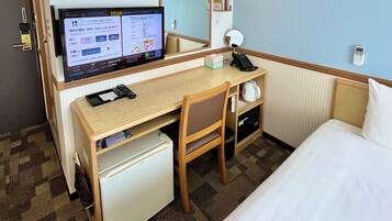 Una habitación de hotel con una cama, un escritorio con computadora, teléfono y un refrigerador pequeño.