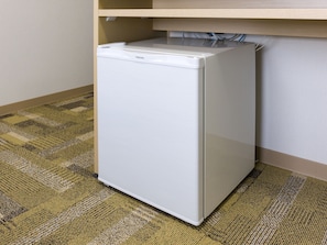 A compact white refrigerator in a corner of a room with a patterned carpet.