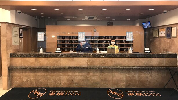 Una recepción de hotel con dos empleados, un reloj y una cámara de seguridad.
