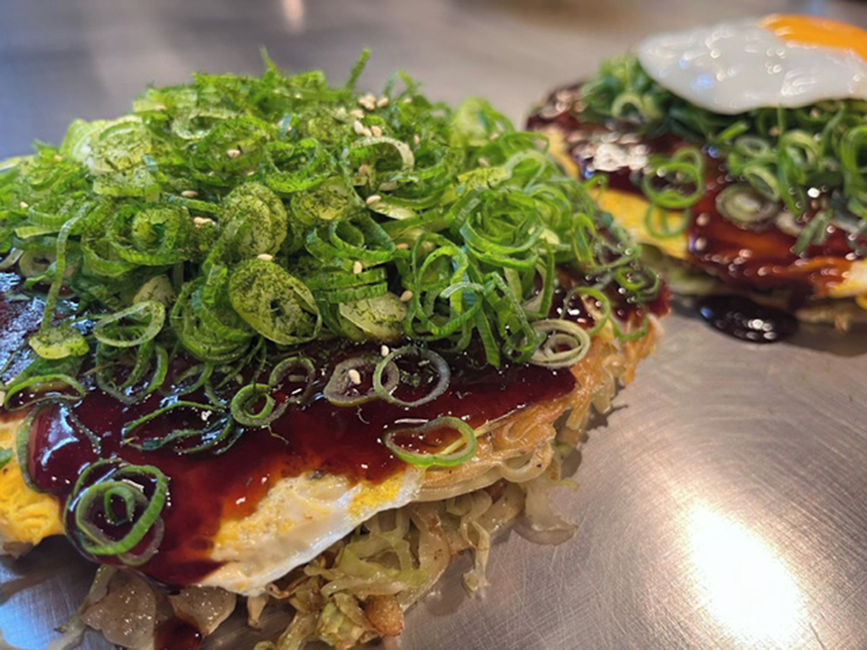 Un plat composé d’un œuf frit, d’oignons verts et d’une sauce foncée, le tout servi dans une assiette en métal.