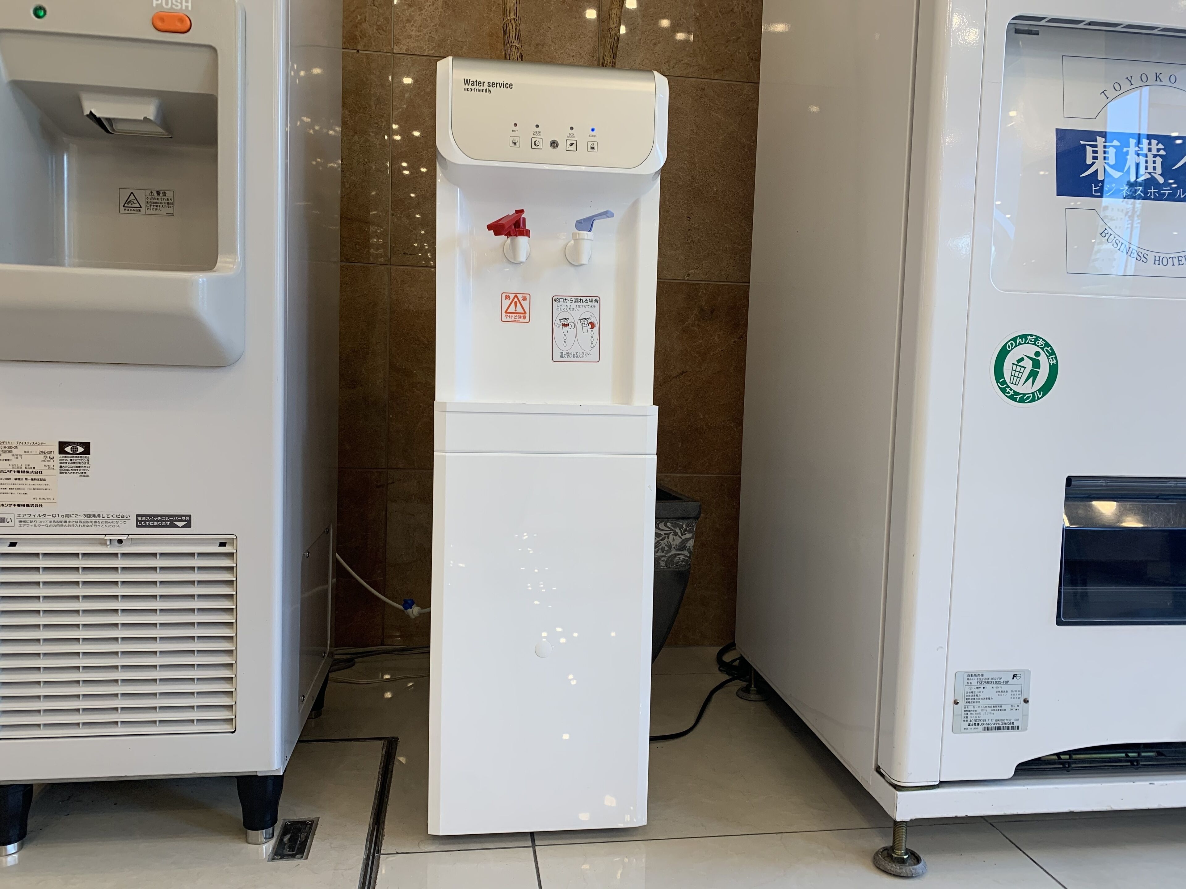 A water dispenser with a push button and a bottle filler, located next to a vending machine.