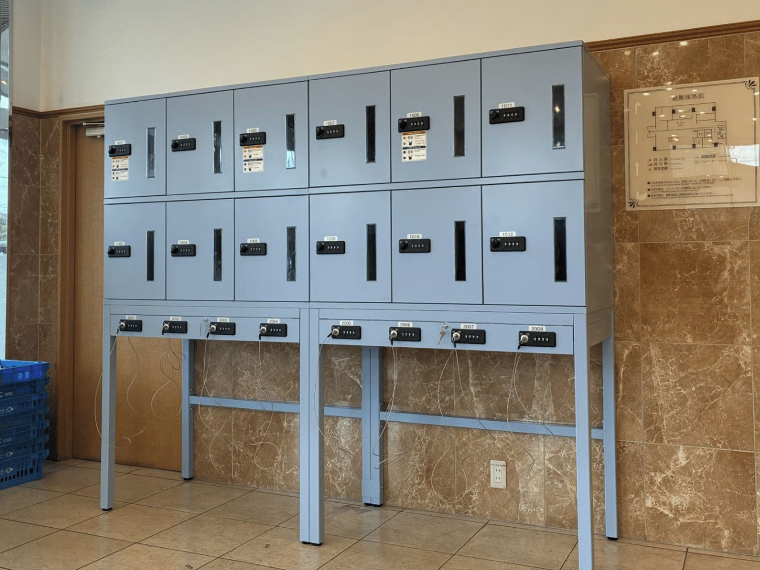A row of blue lockers with numbered labels, a blue cart, and a wall with a floor plan.