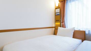Una habitación de hotel con una cama grande, una mesita de noche, una lámpara y una ventana con cortinas.