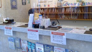 Un mostrador de recepción con folletos informativos, un reloj y un tablón de anuncios con varios avisos.