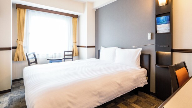 Habitación de hotel con una cama grande, una mesita pequeña, sillas, televisión y una lámpara fijada a la pared.