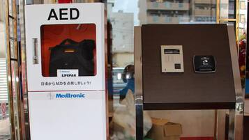 A display of AED devices in a store with a glass door and a view of buildings outside.