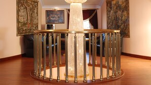 Un gran candelabro con múltiples luces, una mesa redonda con tope de vidrio y dos grandes cuadros enmarcados en las paredes.