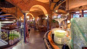 Un restaurante con arcos de ladrillo, mesas de madera y una zona de bar con vasos y botellas.