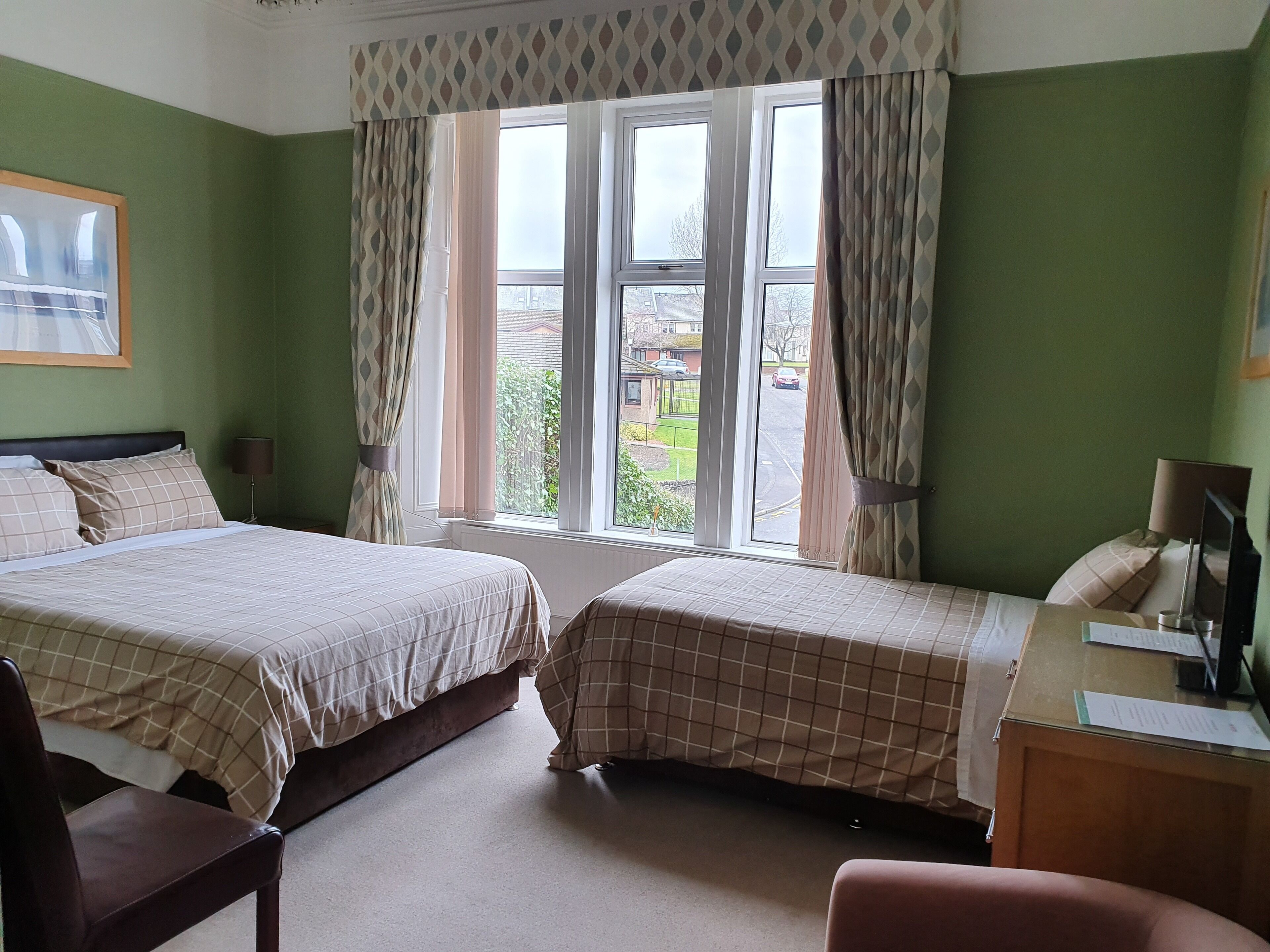 A hotel room with two beds, a desk, a chair, and a window with curtains.