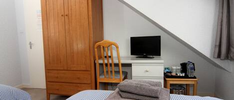 Un dormitorio con una cama, un armario de madera, un escritorio con televisor y una mesita de noche con artículos de aseo.