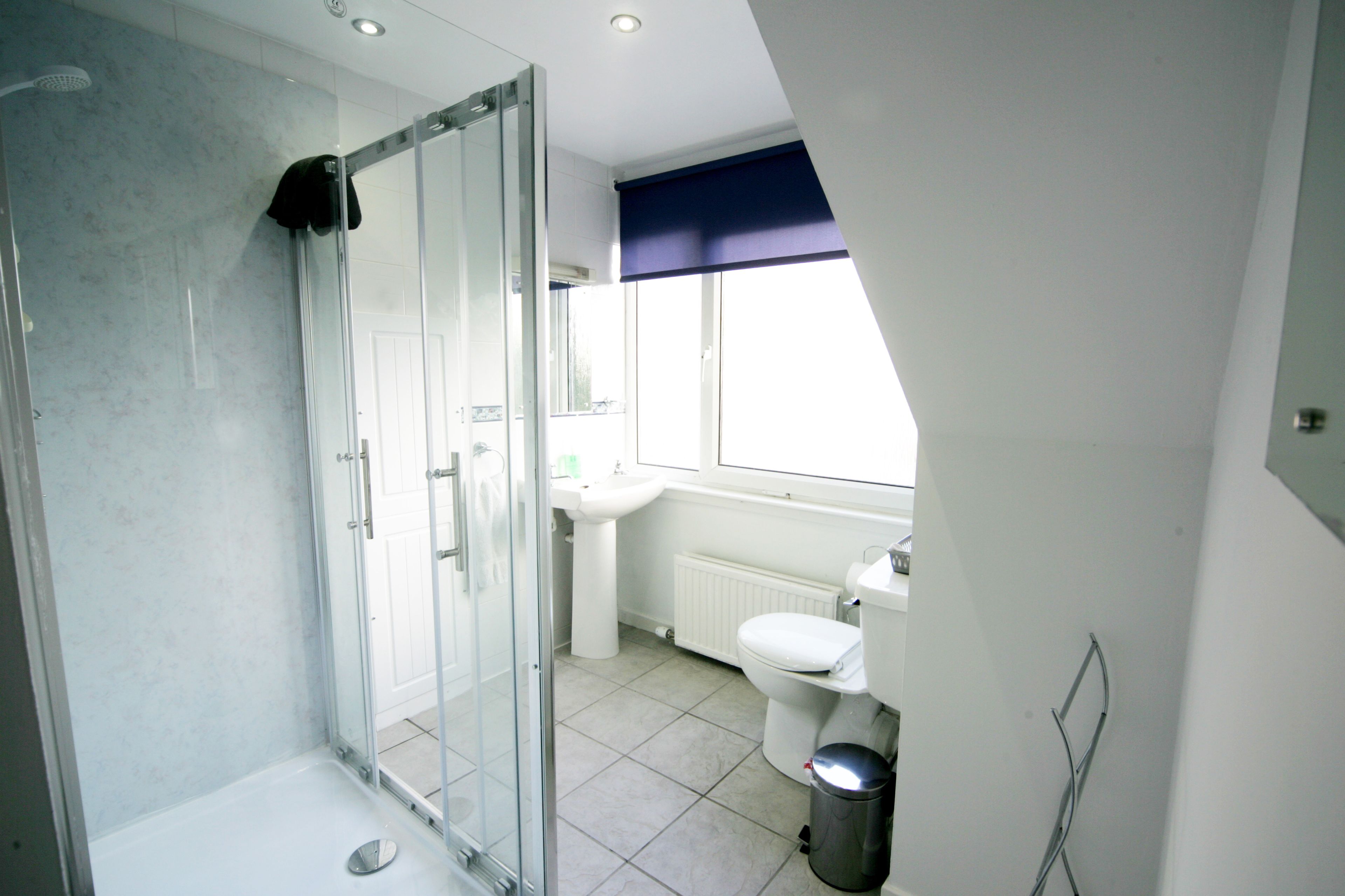 Een moderne badkamer met een douchecabine van glas, een witte wastafel en een toilet.