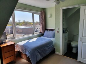 Relax in this serene bedroom with a large window offering a view of the surrounding buildings, a comfortable bed, and a desk for work.