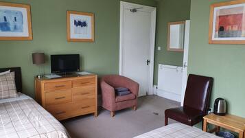 Ein Hotelzimmer mit zwei Betten, einem Holzschrank mit Fernseher, einem pinkfarbenen Sessel, einem braunen Ledersessel und einem kleinen Tisch mit Wasserkocher.