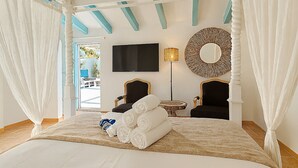 Un dormitorio con una cama, dos sillas, un televisor, un espejo redondo y una ventana con cortinas.