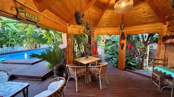 Een houten terras met een zwembad, rieten meubels en een bord waarop 'BEER' staat.
