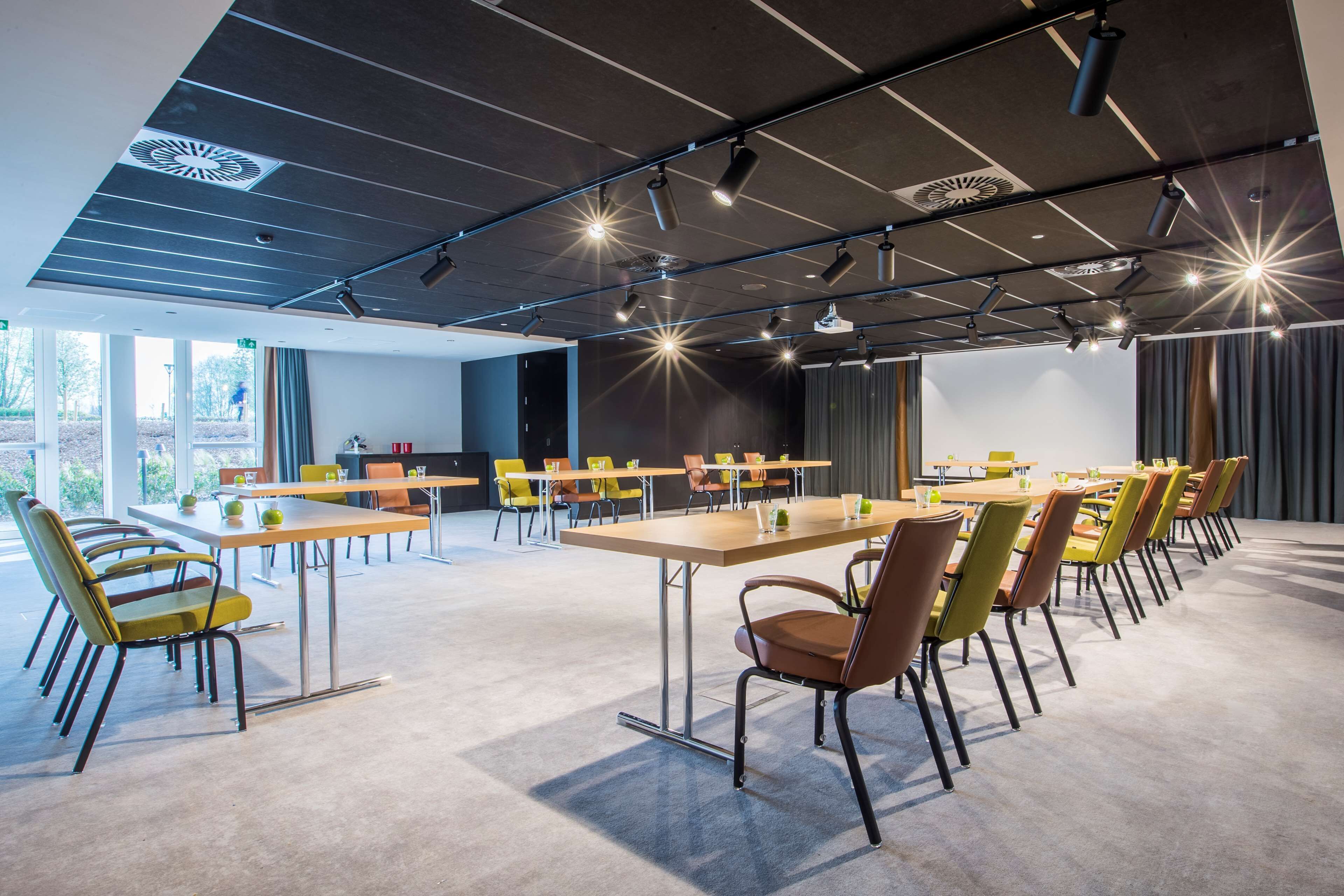 A conference room with multiple tables and chairs, a modern ceiling design, and large windows.