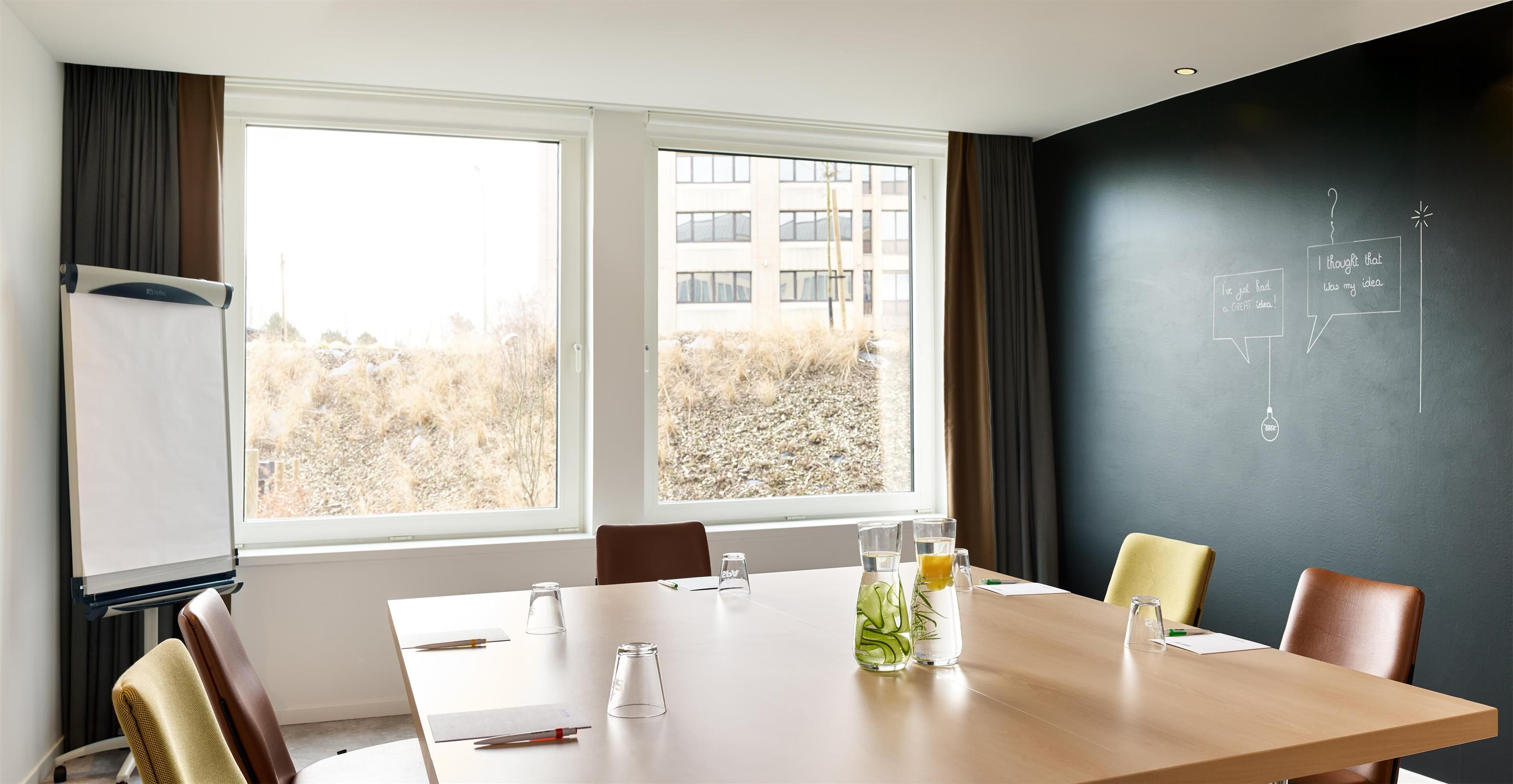 Ein Konferenzraum mit großem Tisch, Stühlen, einer Projektionsleinwand und einer Tafel mit Diagrammen.