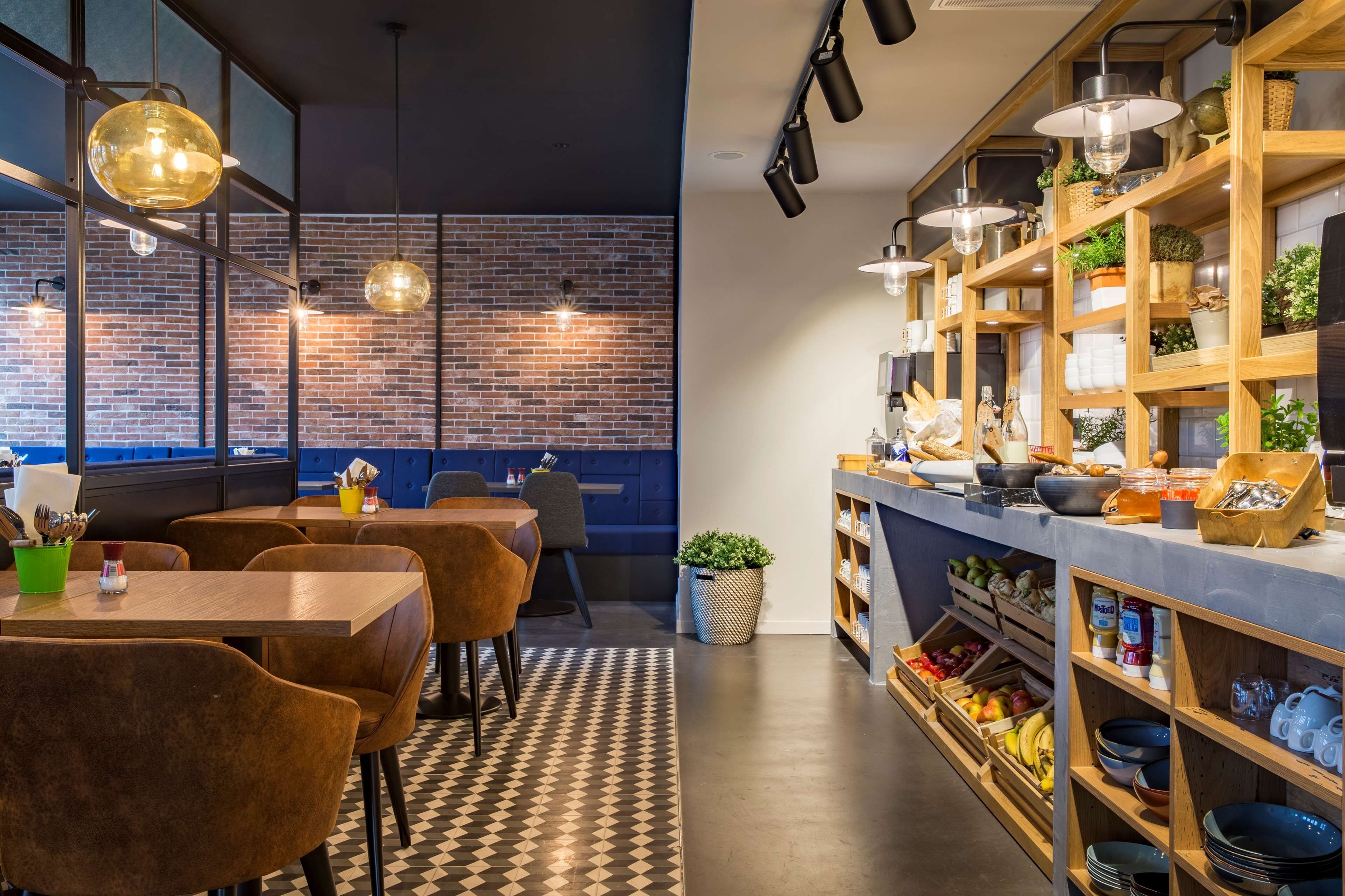 Un restaurant moderne avec des murs en briques, des étagères en bois où sont exposés des produits alimentaires et des chaises en cuir marron.