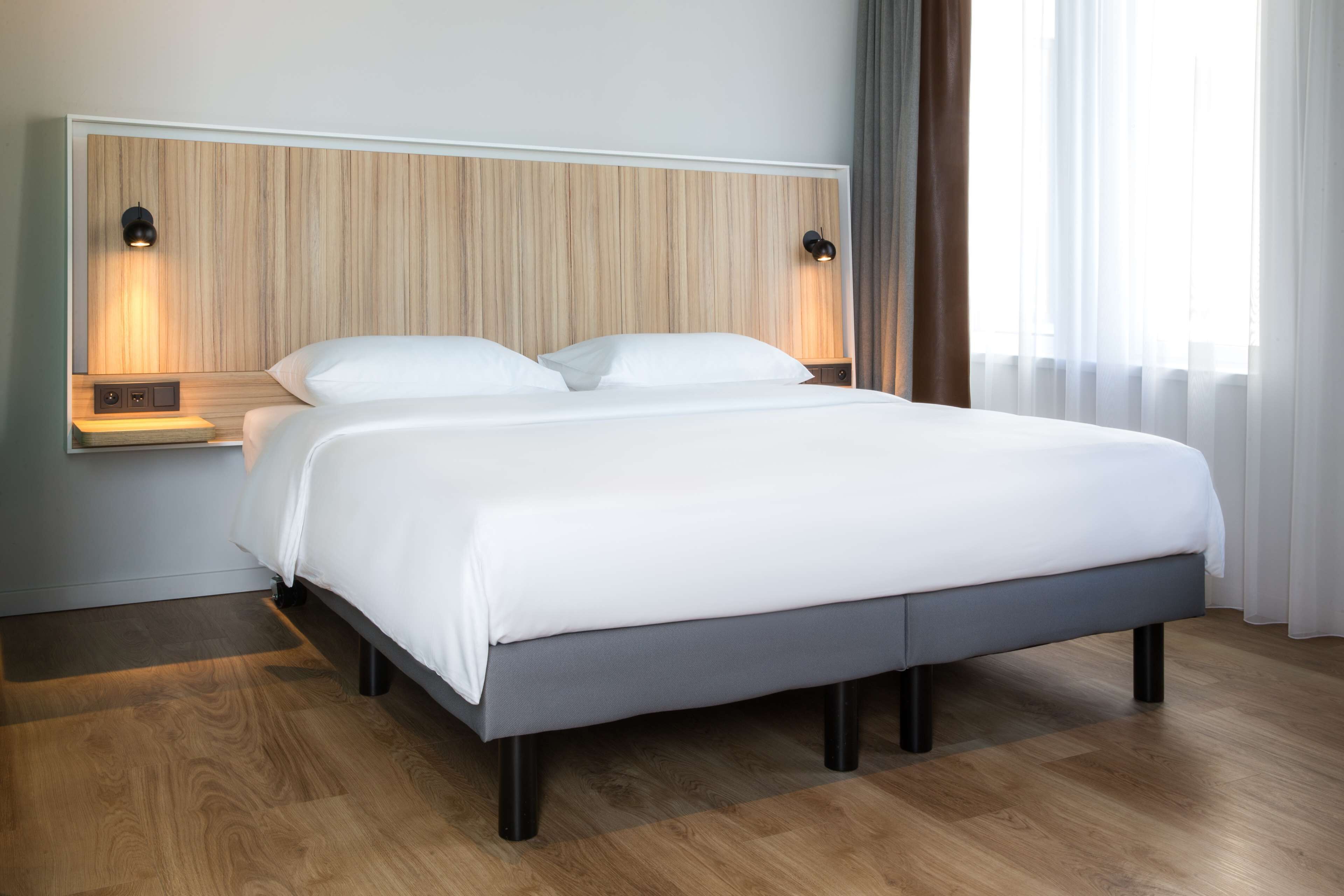 Un dormitorio moderno con cabecera de madera, dos lámparas de noche, una cama grande con ropa blanca y suelo de madera.