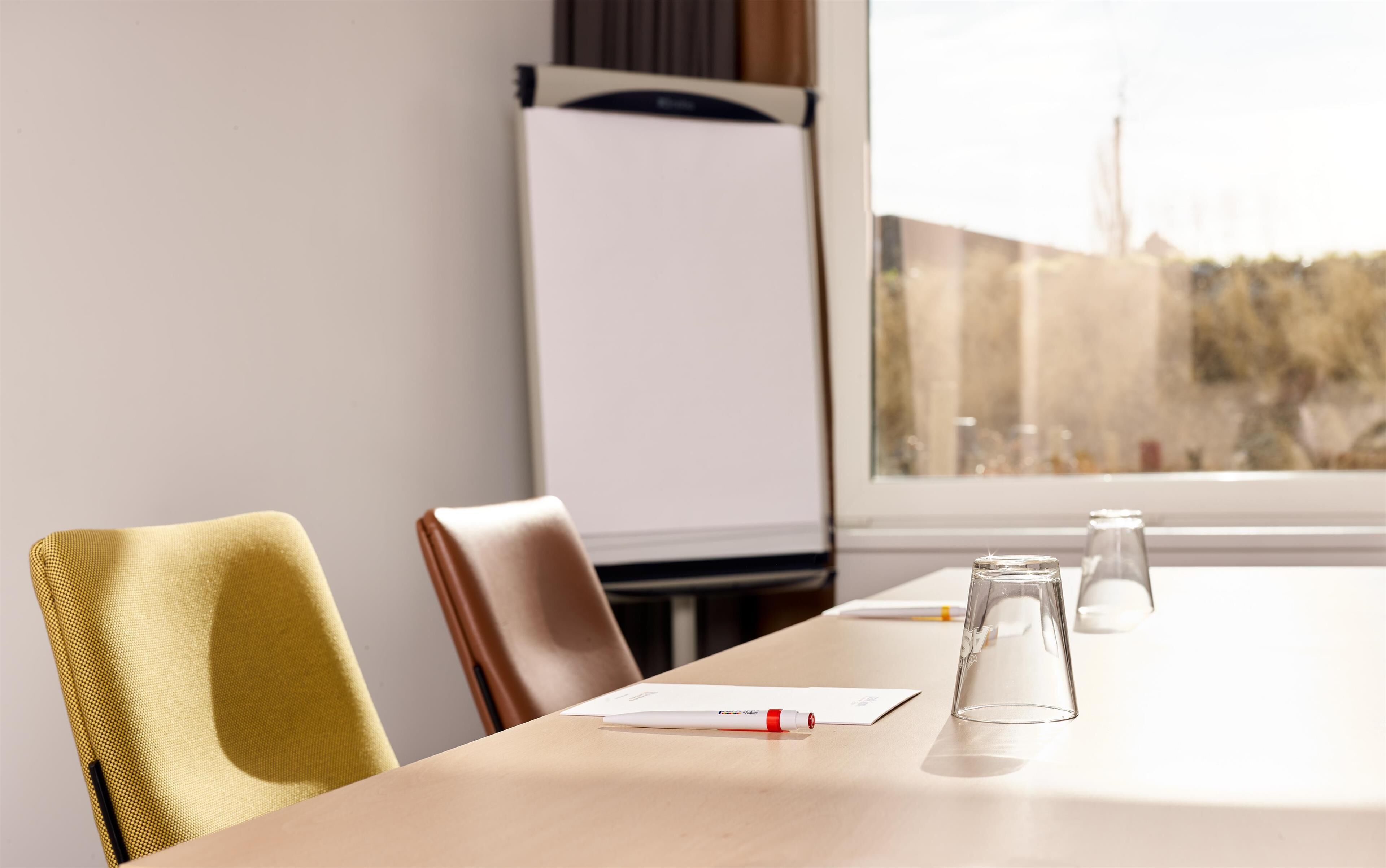 Un salón de conferencias con una pizarra, una mesa de cristal y vistas a árboles a través del ventanal.
