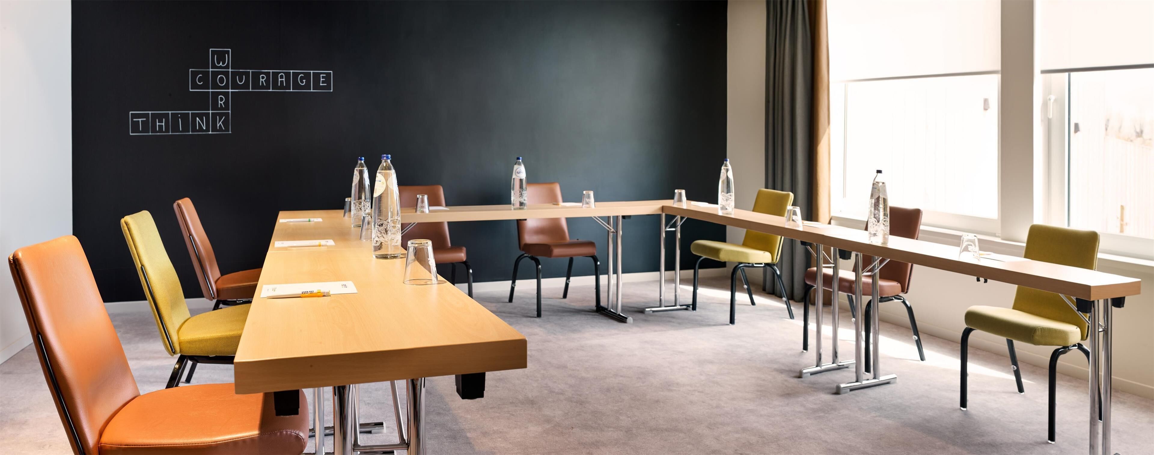 Un salón de conferencias con una larga mesa, múltiples sillas, botellas de agua y una pizarra con palabras motivacionales.