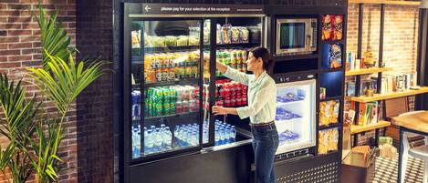 A woman selecting items from a refrigerated display in a store with a 'HUNGRY?' sign above.