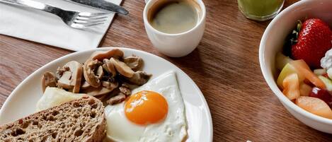 A breakfast setting with plates of eggs, bacon, toast, beans, and a bowl of fruit.