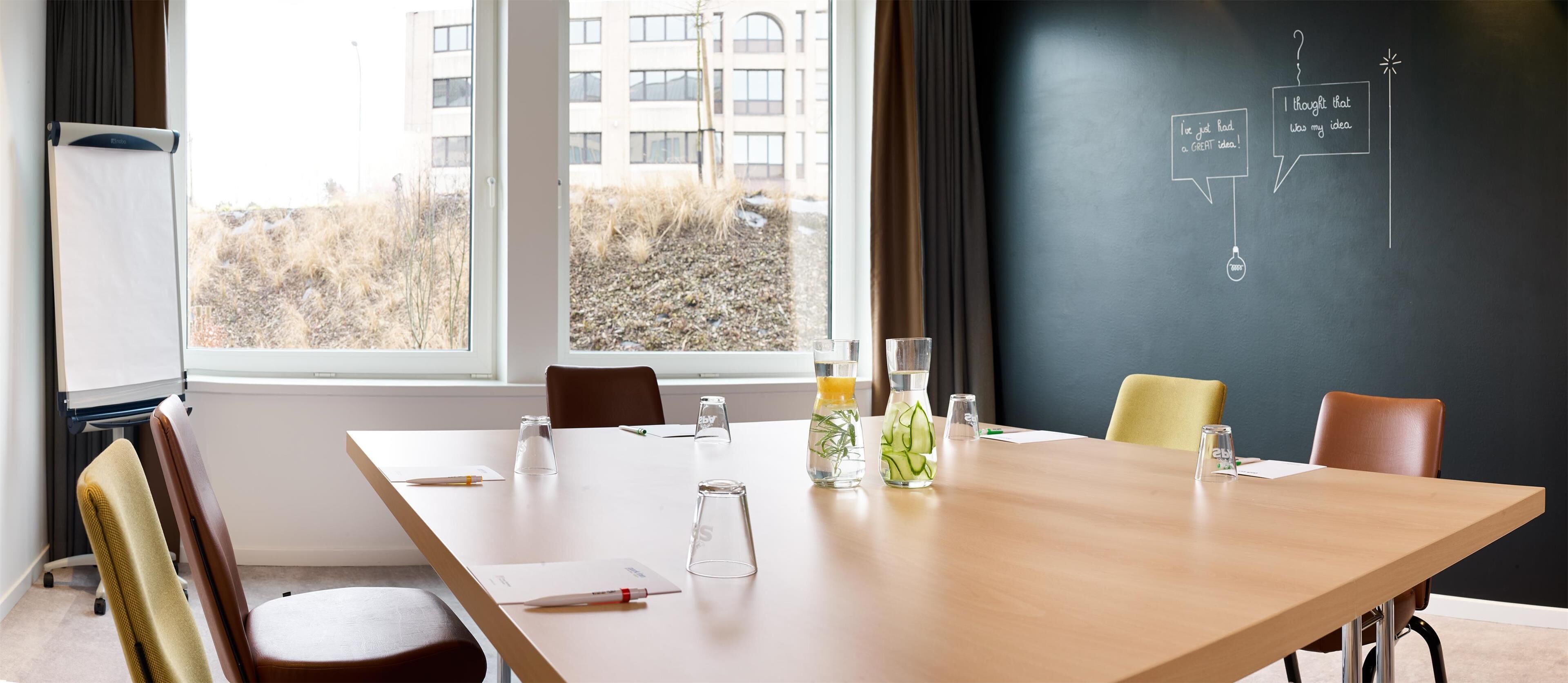 A conference room with a large table, chairs, a whiteboard with diagrams, and a view of buildings outside.