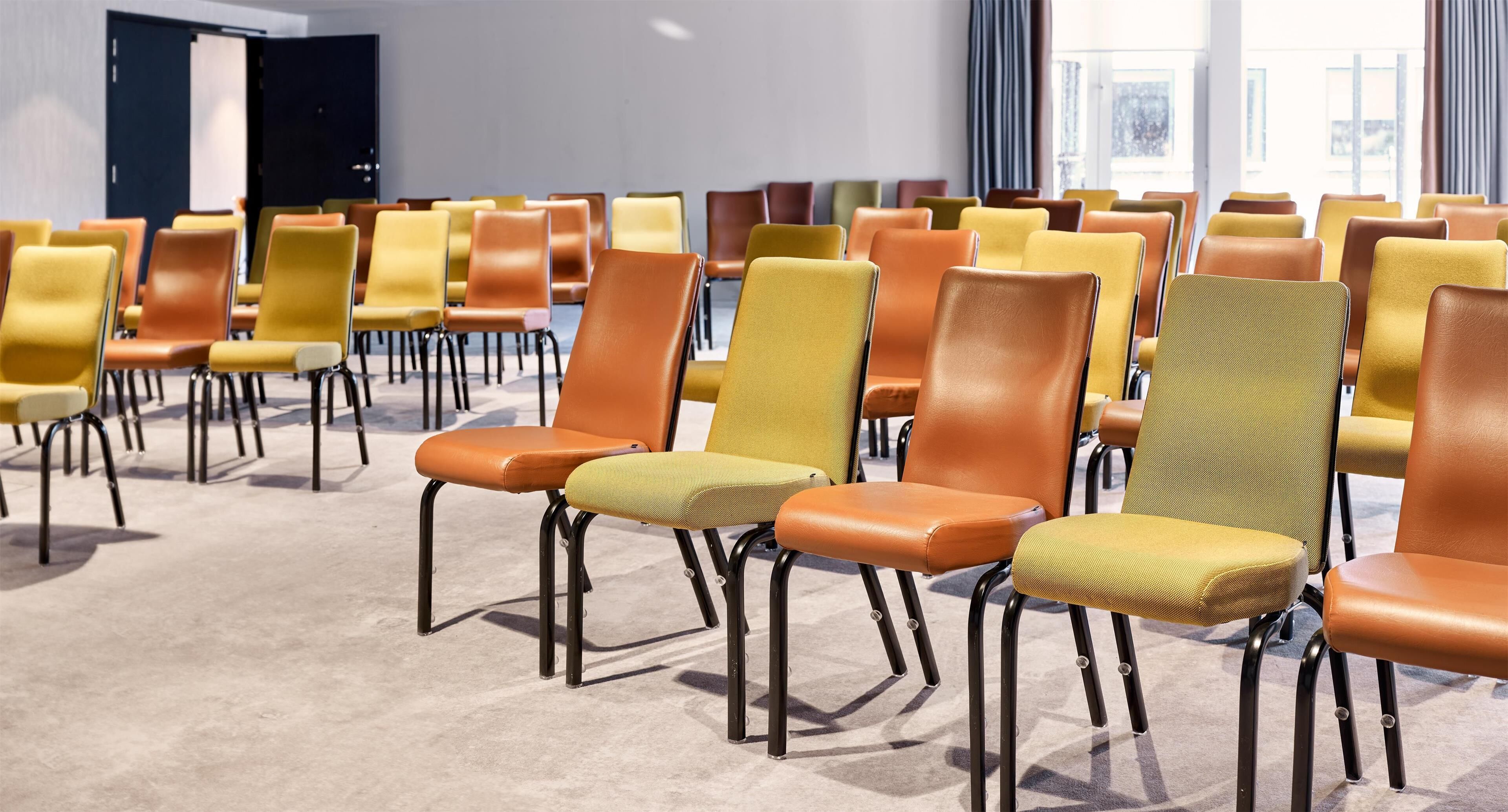 Reihenweise Stühle mit Metallbeinen und gepolsterten Sitzflächen in einem Konferenzraum.