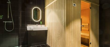 Een moderne badkamer met een houten sauna, een douchecabine van glas en een witte wastafel met spiegel.