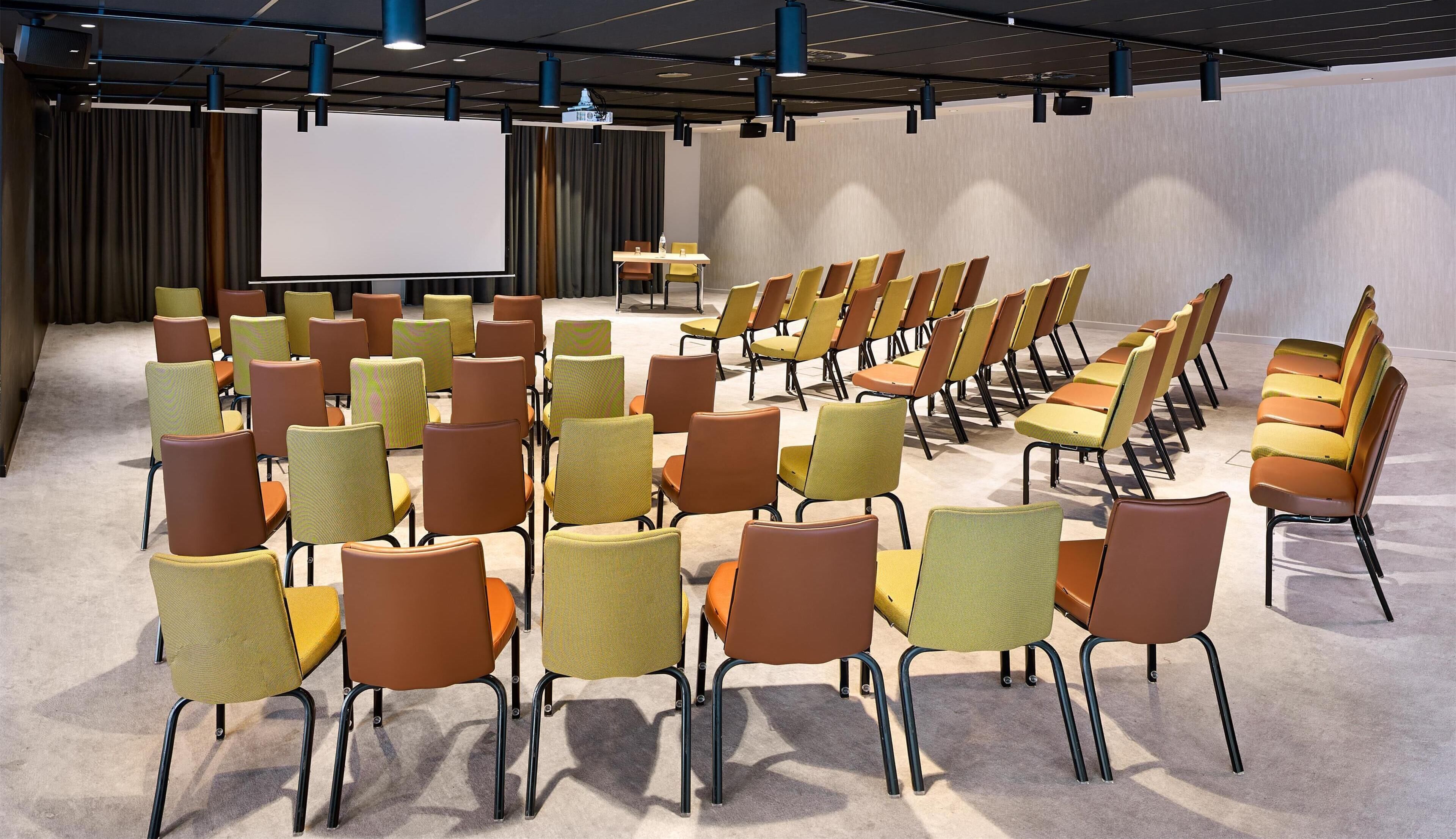 Ein Konferenzraum mit Stuhlreihen, einer Projektionsleinwand und einem Rednerpult.