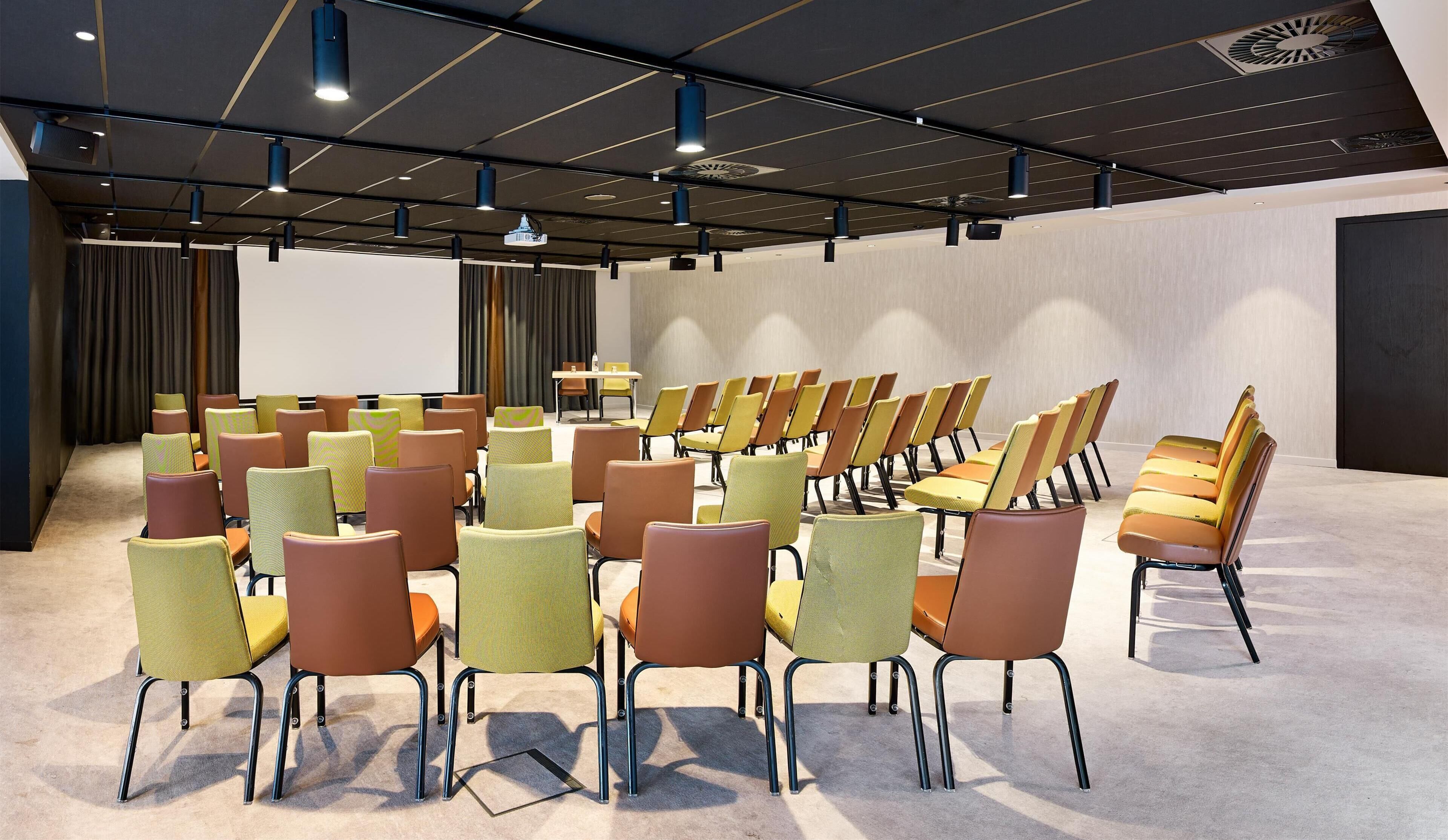 A conference room with rows of chairs, a projector screen, and ceiling lights.