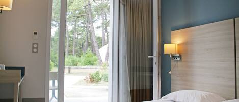 Habitación de hotel con cama, escritorio y puerta corrediza de vidrio que da a un espacio exterior.