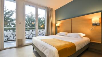 A modern hotel room with a large bed, a wooden headboard, and a view through a sliding glass door to an outdoor balcony.