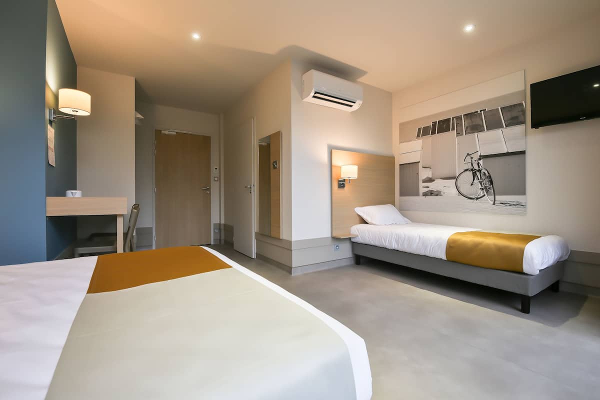 Ein modernes Hotelzimmer mit einem großen Bett, einem kleineren Bett, einem Wand-Fernseher und einem Fahrrad, das an der Wand lehnt.
