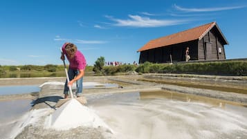 A person working with a shovel in a salt flat area with a wooden building in the background.