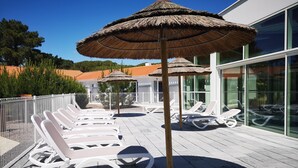 Een terras op het dak met witte lounge fauteuils en rieten parasols, met uitzicht op een schilderachtige omgeving.