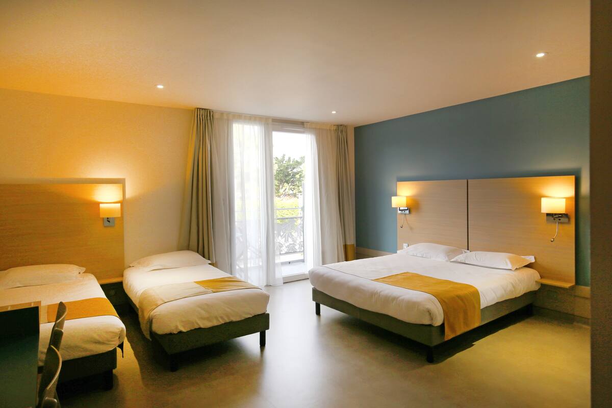 Ein Hotelzimmer mit zwei Betten, einem Schreibtisch und Blick auf Grün.