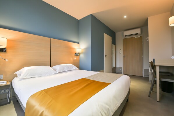 Una habitación de hotel con cama, mesita de noche, lámpara y escritorio con silla.